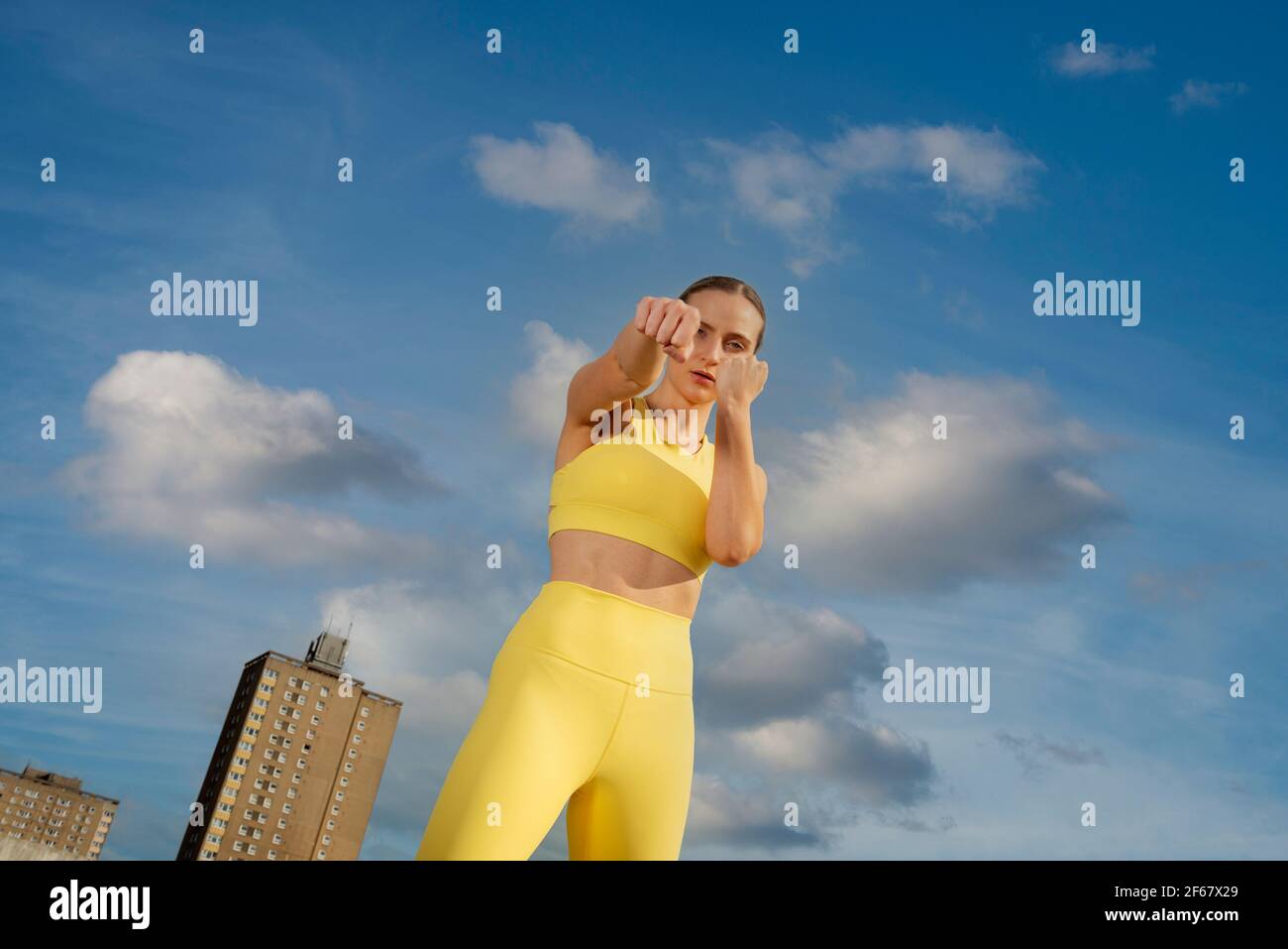 Donna che indossa abiti attivi gialli che si esercitano all'esterno in un ambiente urbano, pugni in su in una posa di boxe. Foto Stock
