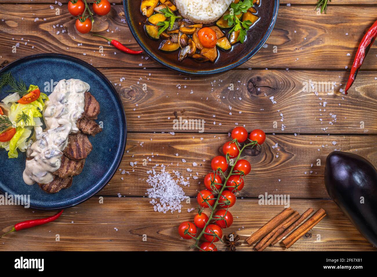 Polpettine di manzo su un piatto con verdure, verdure stufate con riso, lattuga, peperone, rosmarino, aglio e sesamo su fondo di legno marrone. Foto Stock