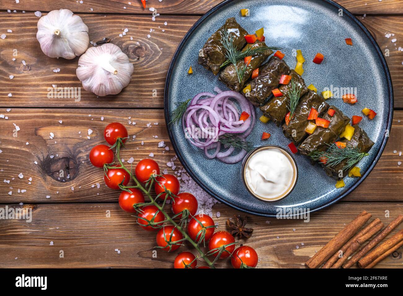 Dolma in foglie d'uva su un piatto su fondo di legno marrone, decorato con spezie, peperoncini, pomodori ciliegini. Un piatto del menu del ristorante. Foto Stock