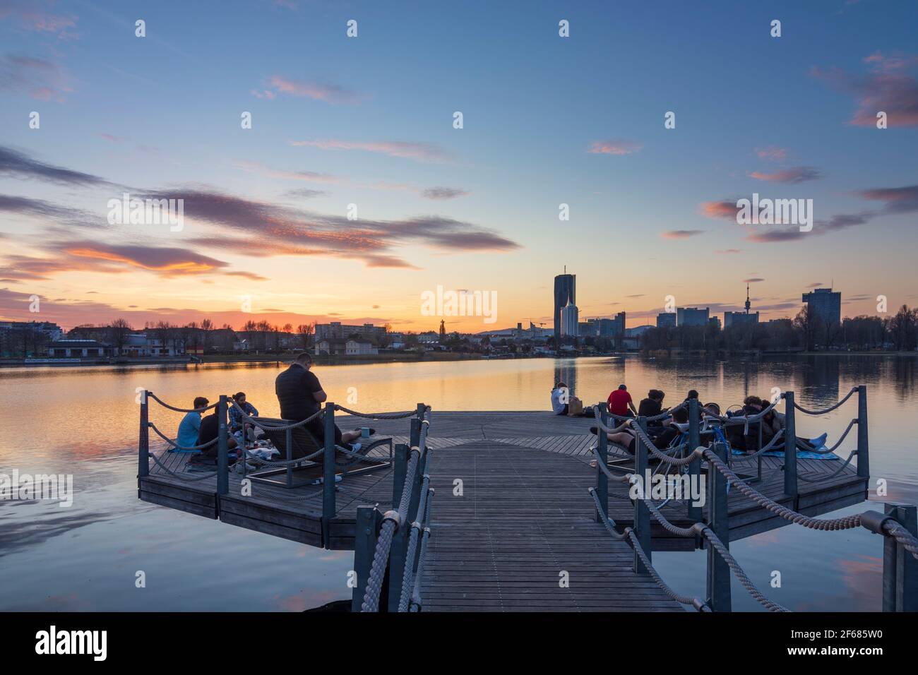 Wien, Vienna: I giovani su una piattaforma in una festa sopra il lago di ossbow Alte Donau (Vecchio Danubio) al tramonto fiero, gli edifici di Donaucity, DC Tower 1, Coro Foto Stock