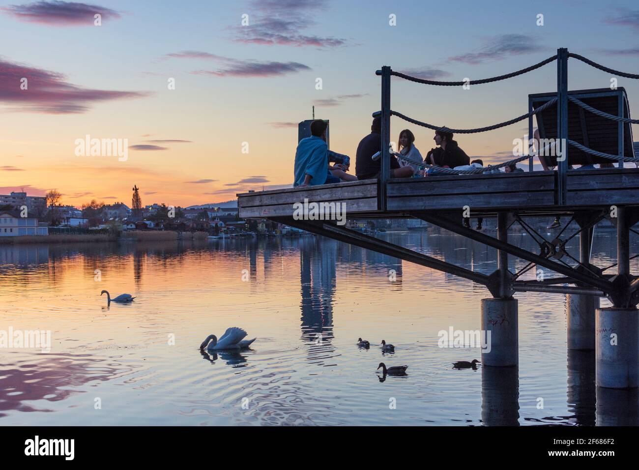 Wien, Vienna: I giovani su una piattaforma in una festa sopra il lago di ossbow Alte Donau (Vecchio Danubio) al tramonto fiero, gli edifici di Donaucity, DC Tower 1, Coro Foto Stock