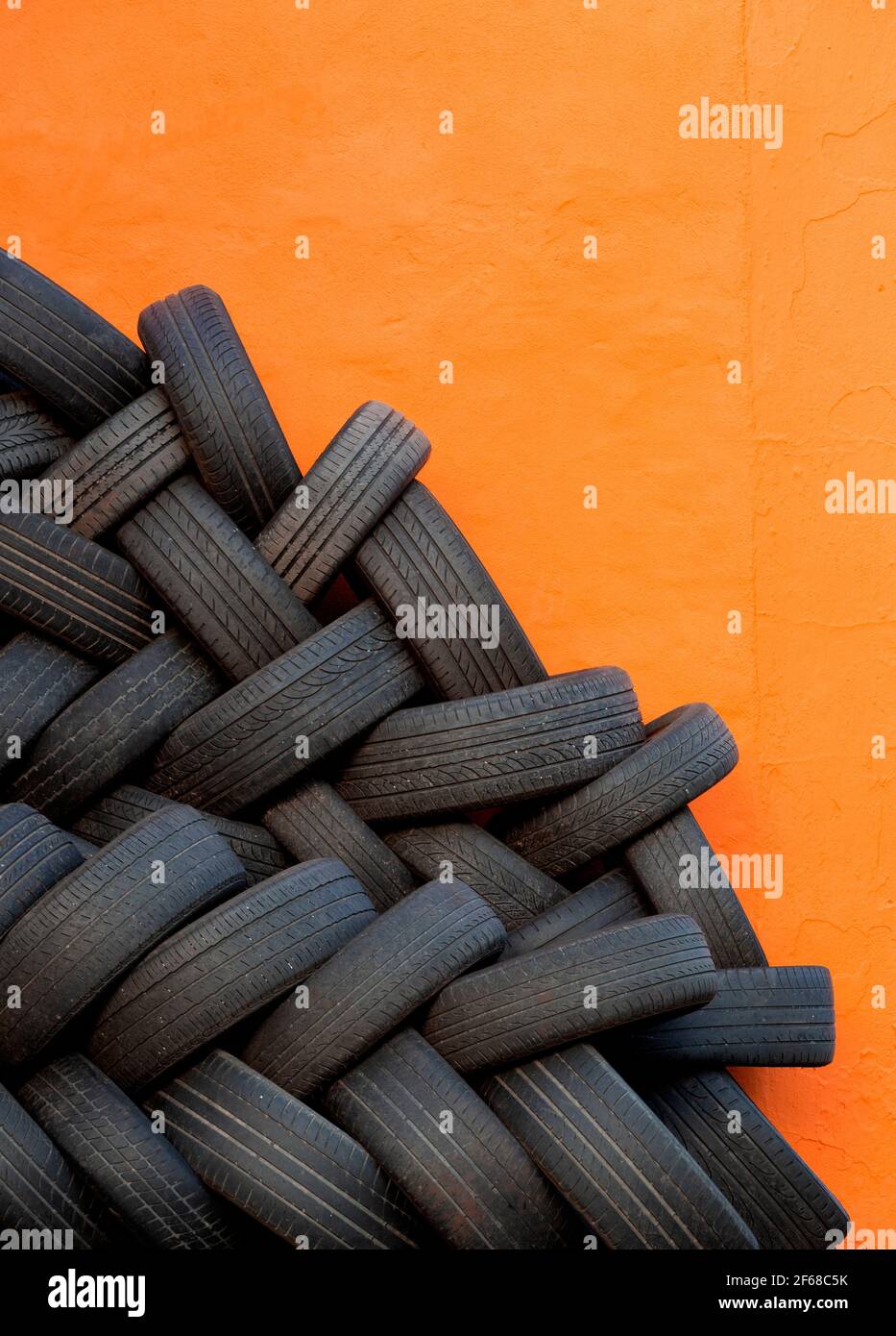 Immagine stradale astratta e colorata di pneumatici per auto usati intrecciati impilati contro una parete di garage in chiaro, dipinto di arancione scuro in attesa di essere riciclata Foto Stock