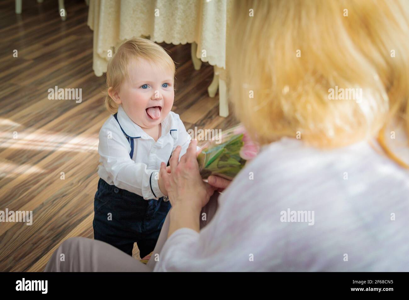Il ragazzino si congratula con la madre per la vacanza, le dà fiori e un regalo. Ragazzo in camicia bianca e pantaloni con sospenditori Foto Stock