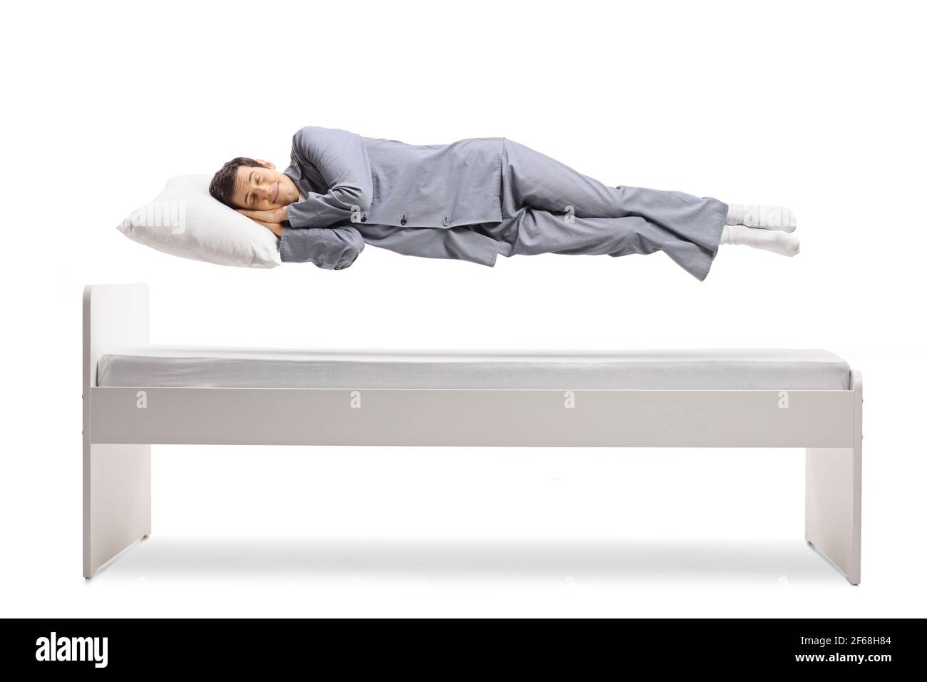 Uomo in pigiama che dorme e galleggia sopra un letto isolato su sfondo bianco Foto Stock