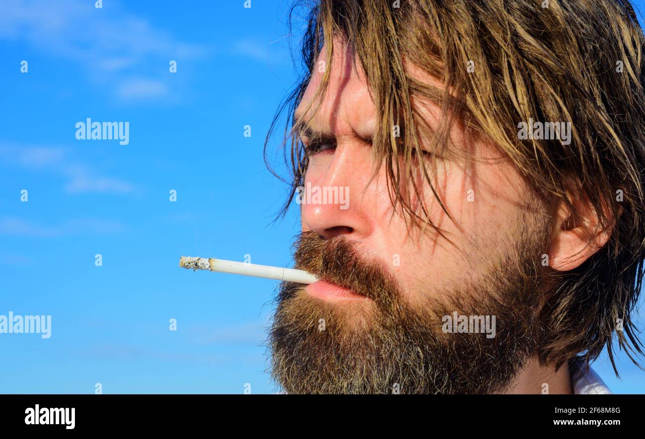 Uomo bearded fumando Cigarette all'aperto. Brutale ragazzo che fuma tabacco. Cannabis medica. Foto Stock