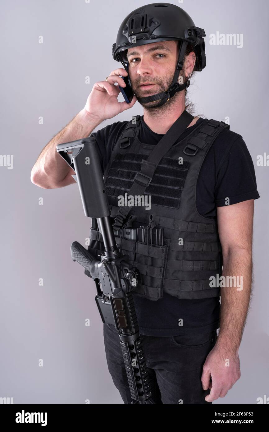 Uomo equipaggiato per Airsoft con casco e gilet protettivo sta parlando al telefono mentre si sta in piedi con la sua arma visualizzata. Le comunicazioni sono importanti Foto Stock