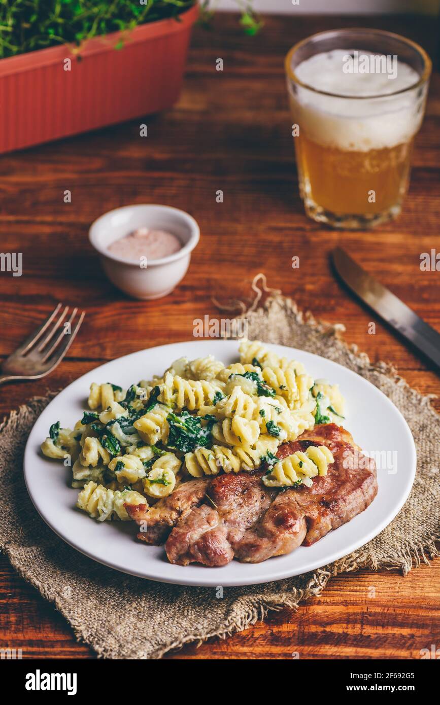 Bistecca di maiale con spinaci cremosi di pasta guarnita con grattugiata Parmigiano su piatto bianco Foto Stock