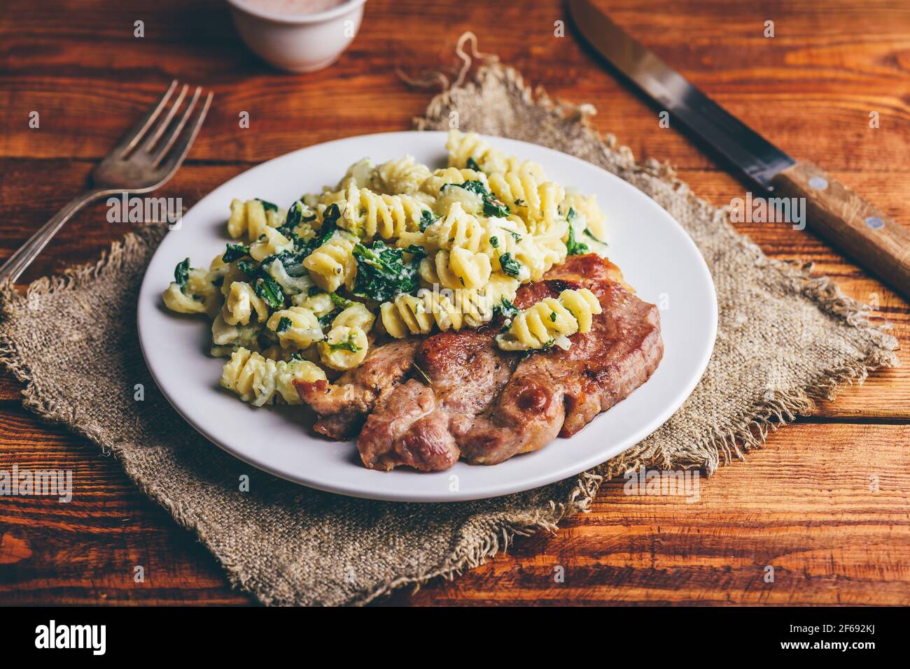 Bistecca al collo di maiale e pasta cremosa con spinaci e timo Guarnito con parmigiano grattugiato su piatto bianco Foto Stock