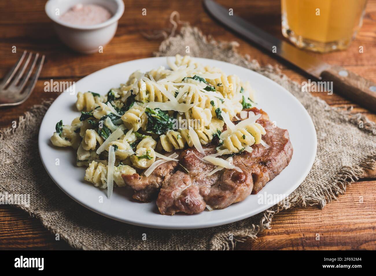 Bistecca di maiale con spinaci cremosi di pasta guarnita con grattugiata Parmigiano su piatto bianco Foto Stock