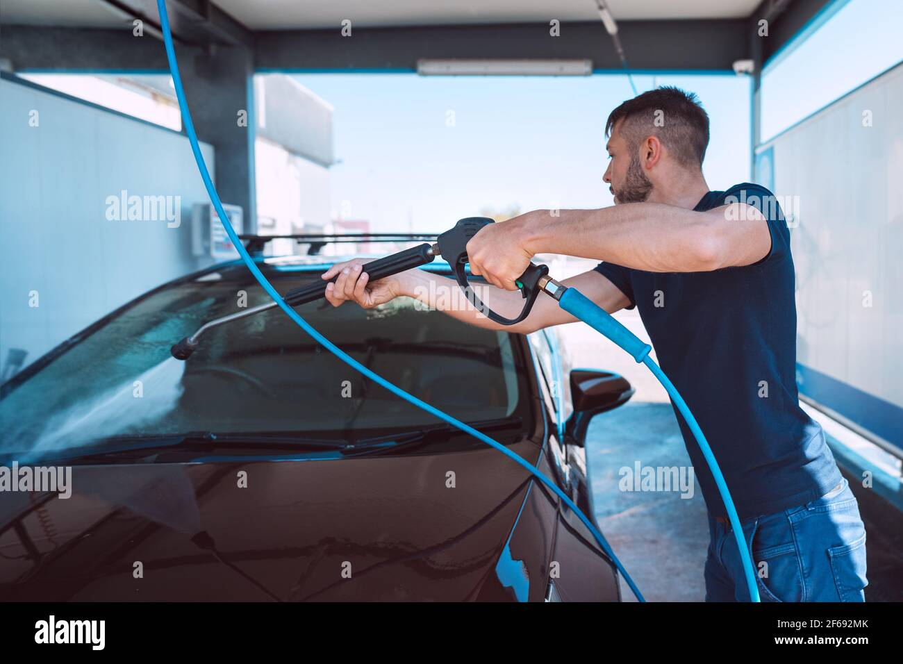 Uomo che lava la sua moderna auto marrone in autolavaggio self-service. Pulizia dell'auto con acqua ad alta pressione. Autolavaggio intelligente Foto Stock