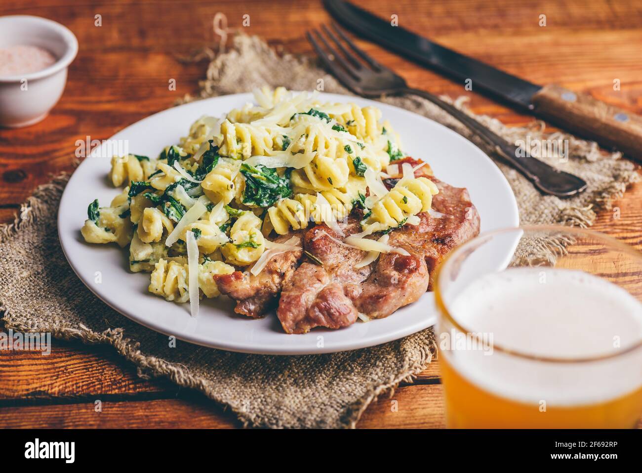 Bistecca di maiale fritta e pasta di spinaci con ricotta e parmigiano Formaggio su piatto bianco Foto Stock