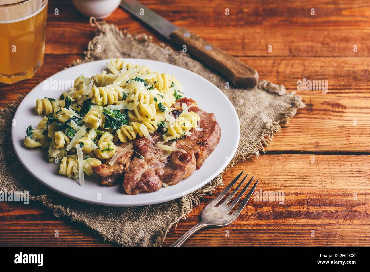 Bistecca di maiale con spinaci cremosi di pasta guarnita con grattugiata Parmigiano su piatto bianco Foto Stock