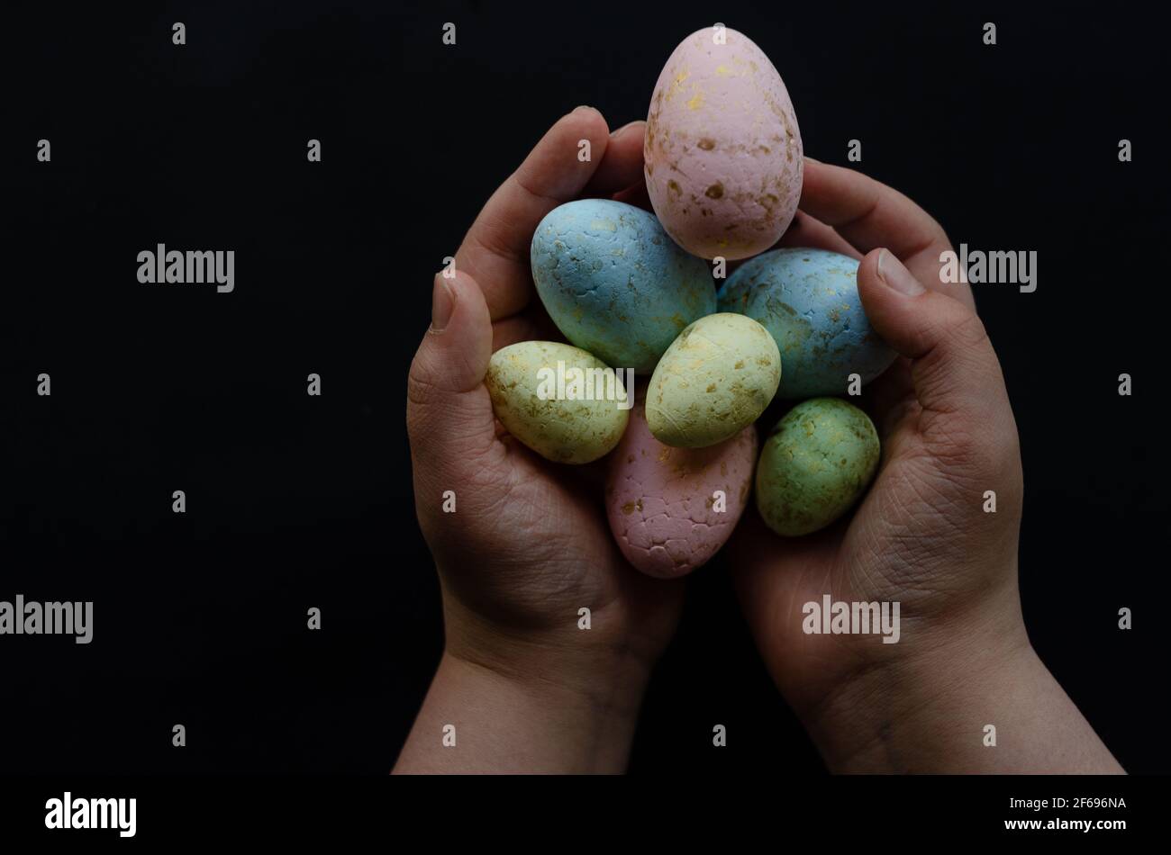 Uova di Pasqua in mani su sfondo nero, spazio libero Foto Stock