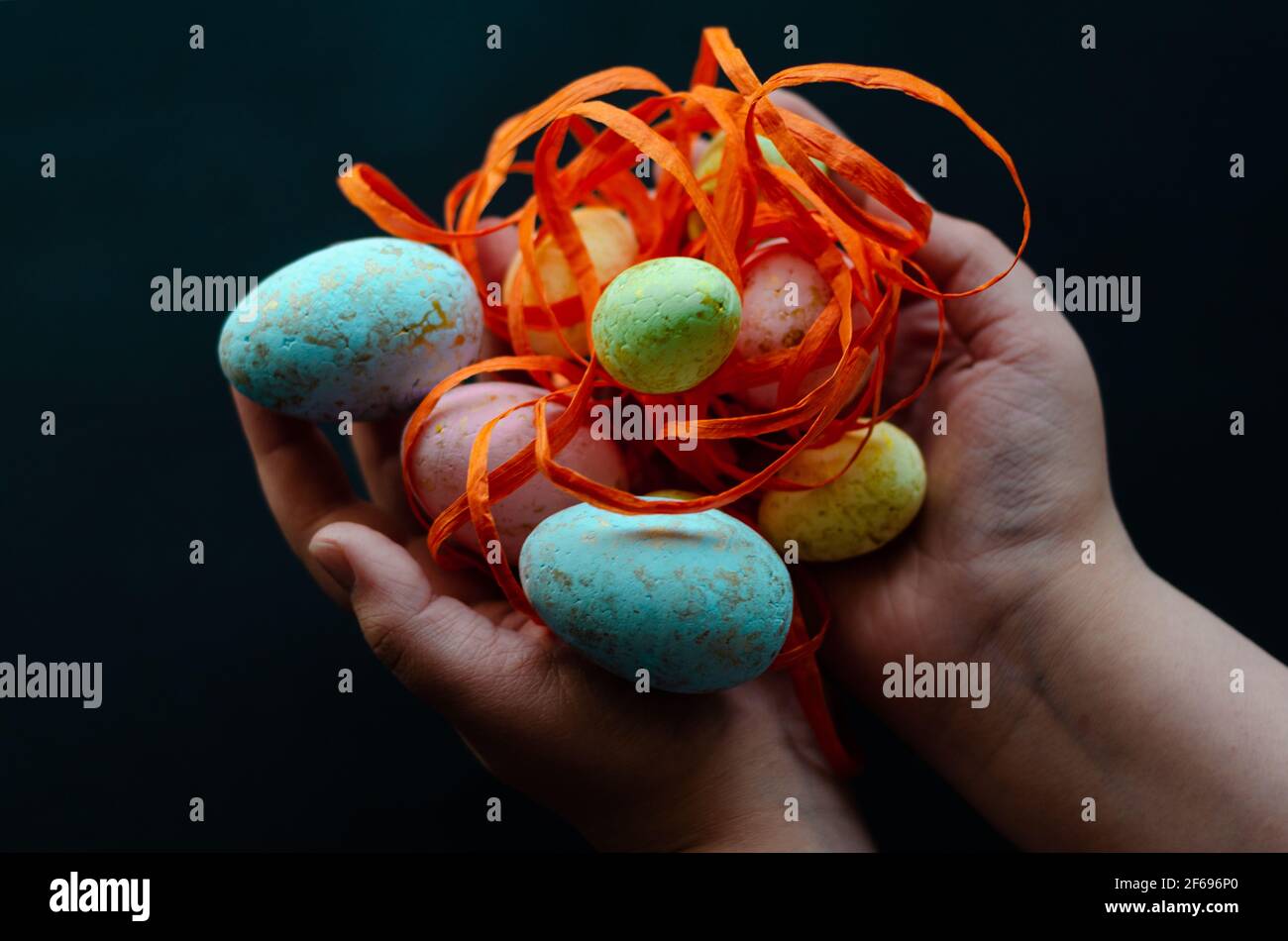 uova di pasqua con nastro arancione in mani su sfondo scuro, spazio libero Foto Stock
