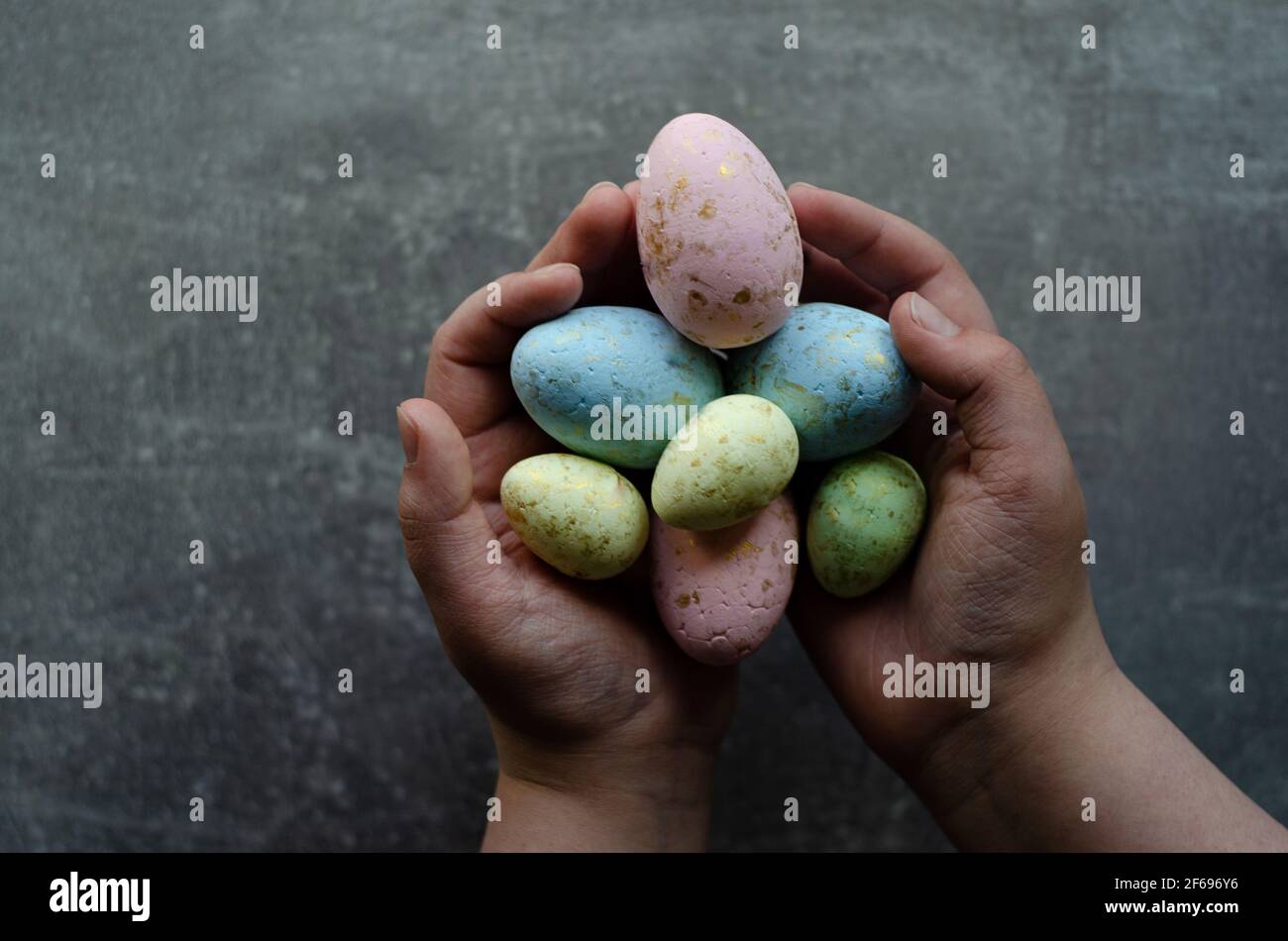 Uova colorate di Pasqua in mani su sfondo grigio, posto libero Foto Stock
