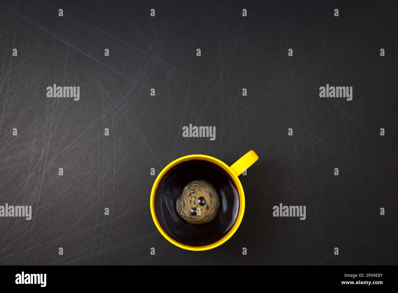 Mescolare in senso orario. Tazza gialla di caffè nero piatto posare su fondo nero graffiato ruvido. Consente di copiare lo spazio per il testo, l'immagine o il messaggio. Vista dall'alto minima. Foto Stock