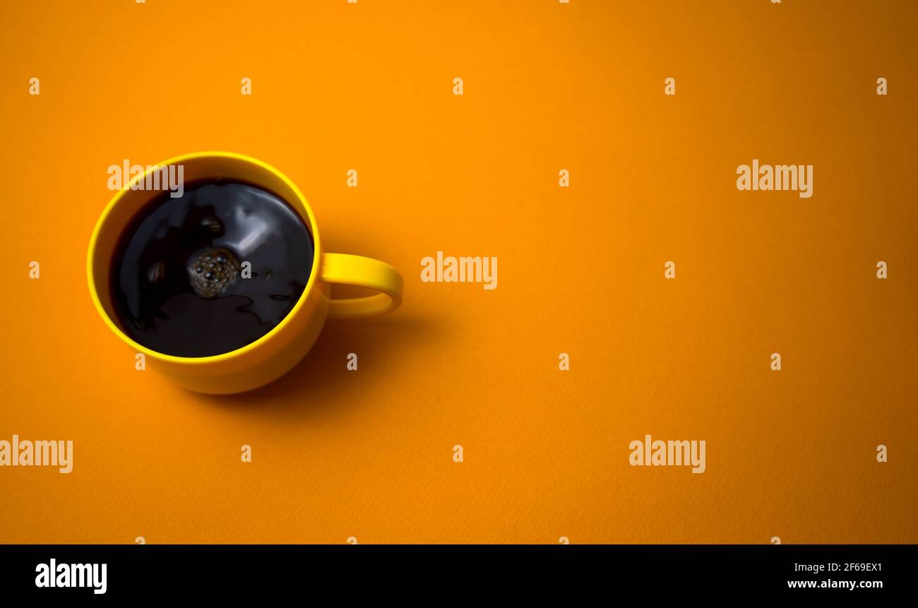 Tazza gialla di caffè nero strring piatto posare su sfondo di colore giallo scuro. Consente di copiare lo spazio per il testo, l'immagine o il messaggio. Minimo, vista dall'alto, orizzontale. Foto Stock