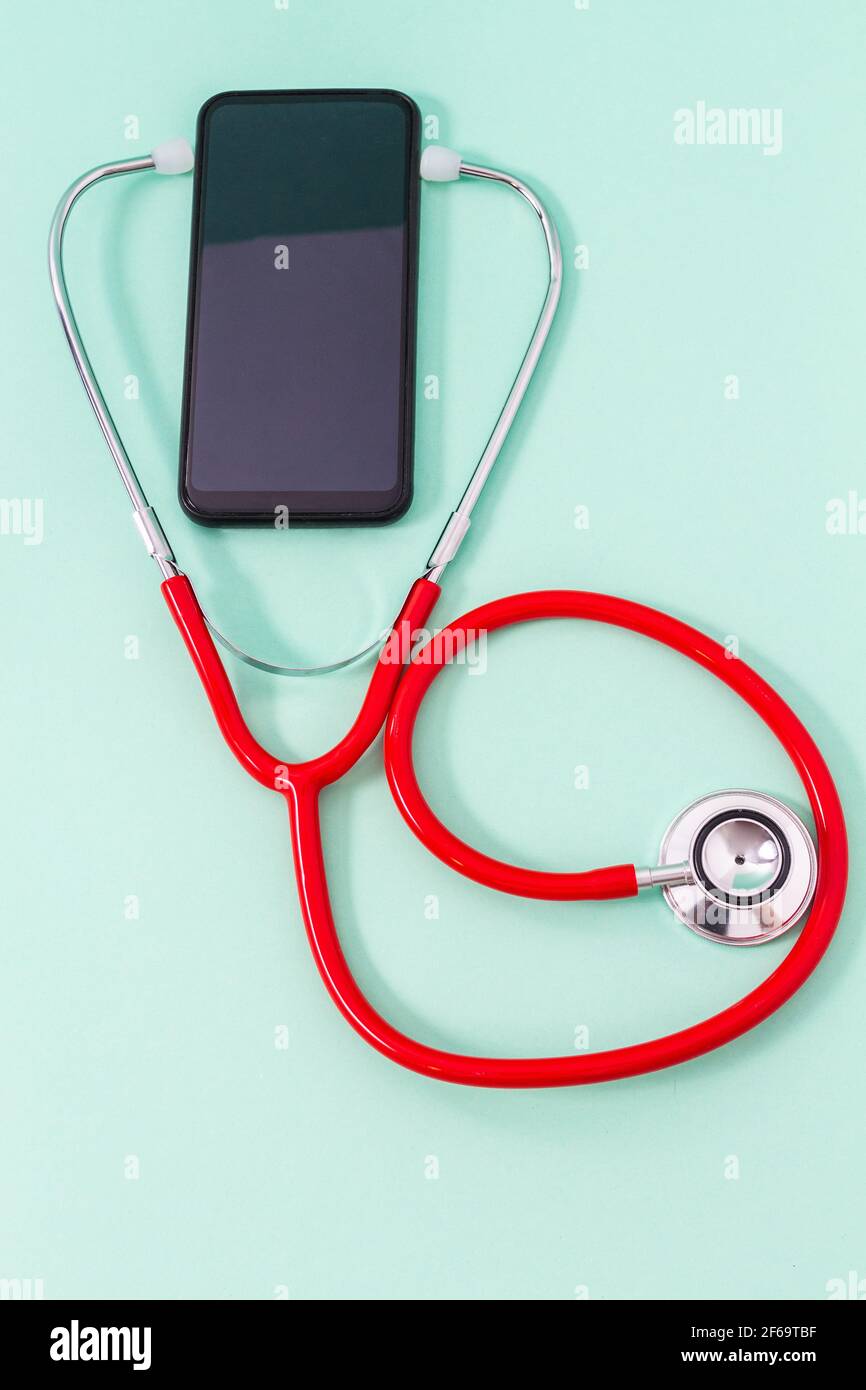 Vista dall'alto di uno stetoscopio in un auricolare per smartphone su sfondo verde acquamarina. Concetto di medicina, comunicazione e tecnologia. Foto Stock