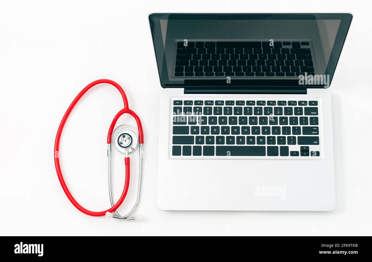 Stetoscopio rosso arrotolato accanto a un computer portatile con aperto monitor isolato su sfondo bianco Foto Stock