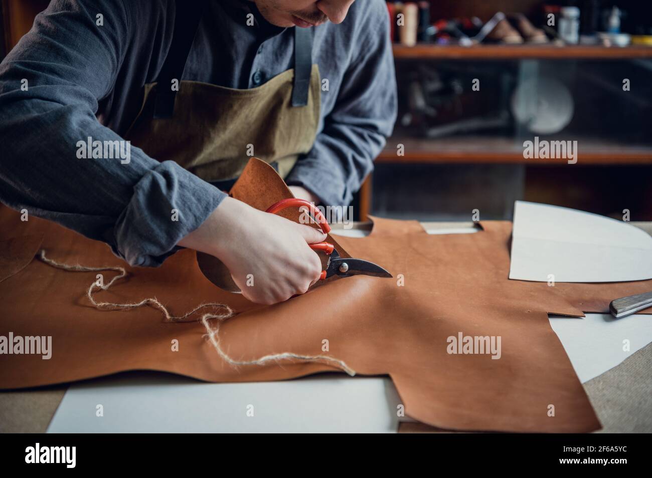 Un giovane ragazzo di talento aiuta suo padre nel commercio di famiglia, taglia fuori gli sbozzi per le scarpe dalla pelle. Foto Stock