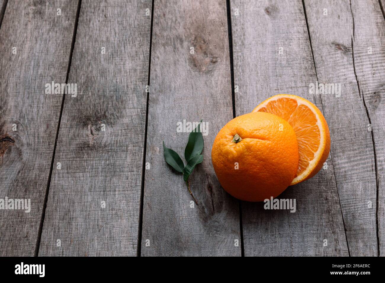 Posa piatta con metà di frutta arancione a fette fresche e mature su sfondo grigio di legno. Polpa di arancia e foglie verdi. Concetto di cibo tropicale. Mangiare sano co Foto Stock