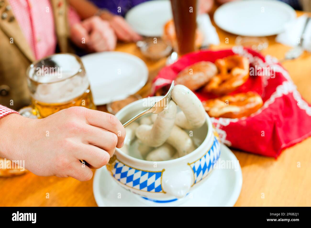 Un gruppo di giovani uomini e donne nelle tradizionali bavaresi Tracht avente una prima colazione con bianco salsiccia di vitello, pretzel e birra Foto Stock