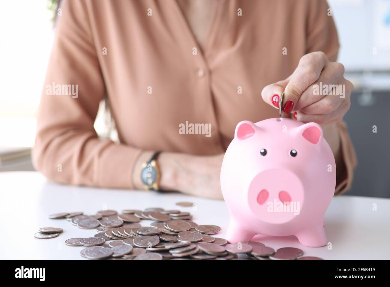 Mano di donna che mette la moneta nel guardaroba rosa della banca del piggy Foto Stock