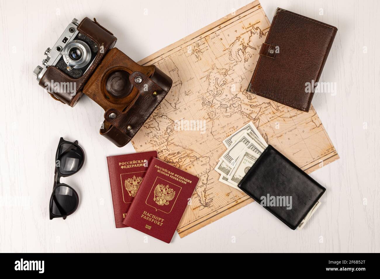 mappa del mondo, due passaporti, denaro in un portafoglio in pelle nera, una vecchia macchina fotografica in una custodia in pelle e occhiali da sole su un tavolo di legno bianco. vista da abov Foto Stock