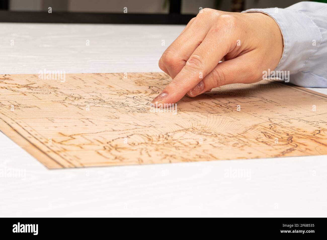 la mano femminile mostra il luogo di viaggio sulla mappa del mondo sullo sfondo di un tavolo di legno bianco. primo piano. fuoco selettivo Foto Stock