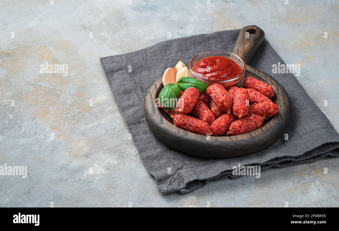 Piccole salsicce affumicate con picolini all'aglio e basilico su fondo grigio. Foto Stock