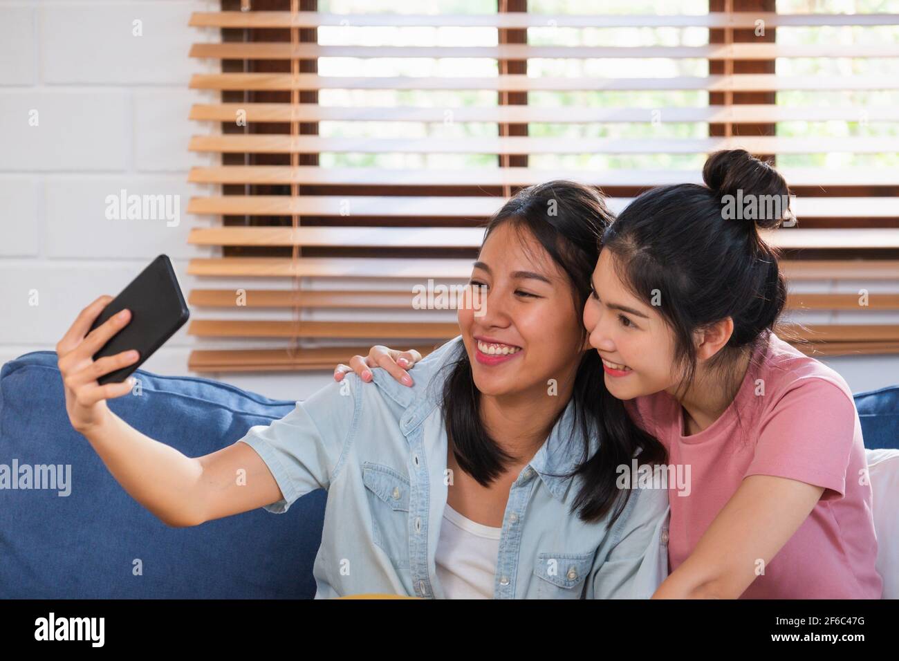 Felice coppia lesbica asiatica utilizzando la videochiamata mobile con un amico sul divano nel soggiorno in casa accogliente Foto Stock