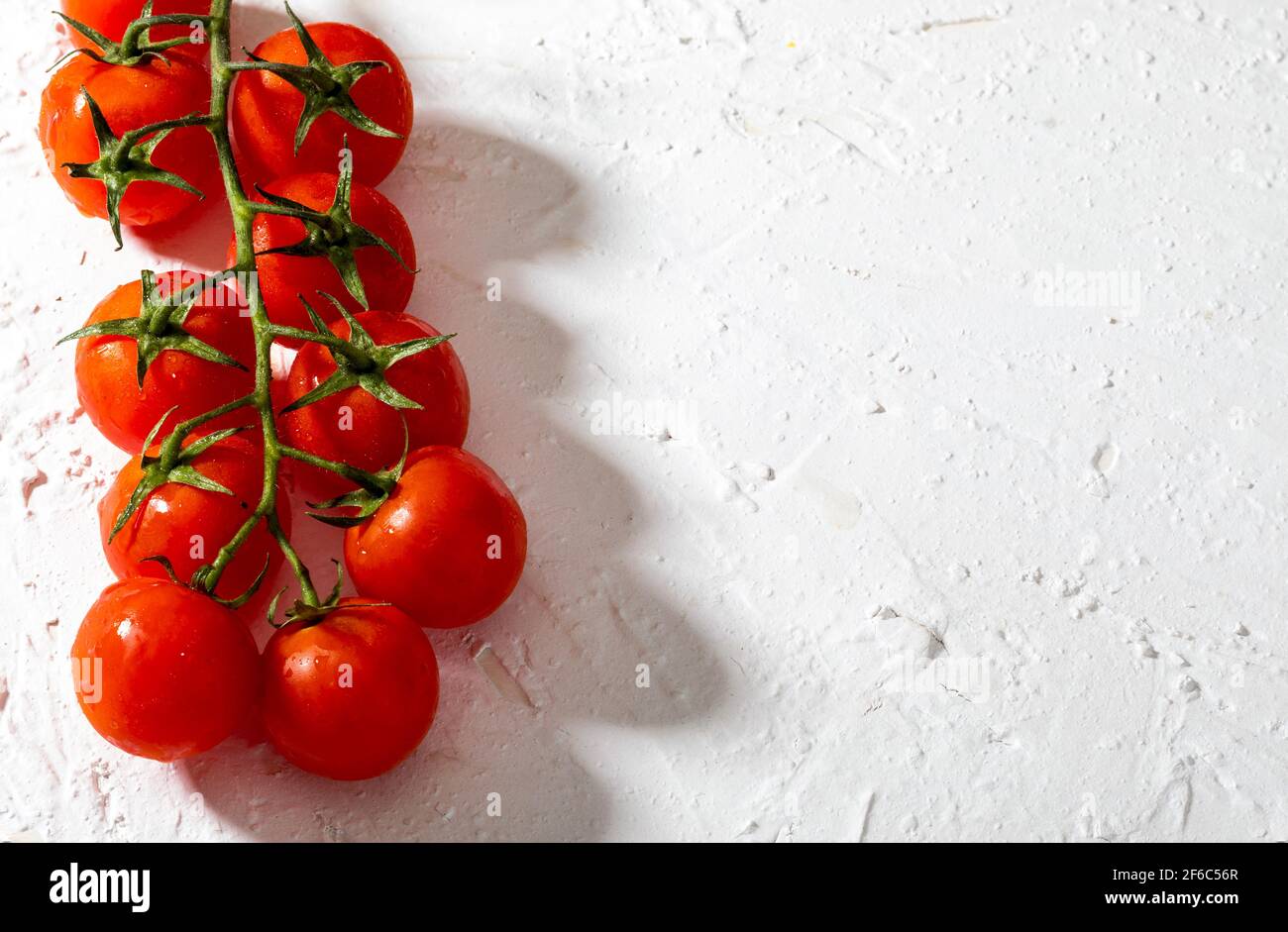 Bei pomodori freschi di vite (ciliegia) con gocce d'acqua, crudi, interi e dimezzati. Su sfondo bianco con texture. Ingredienti della dieta mediterranea Foto Stock