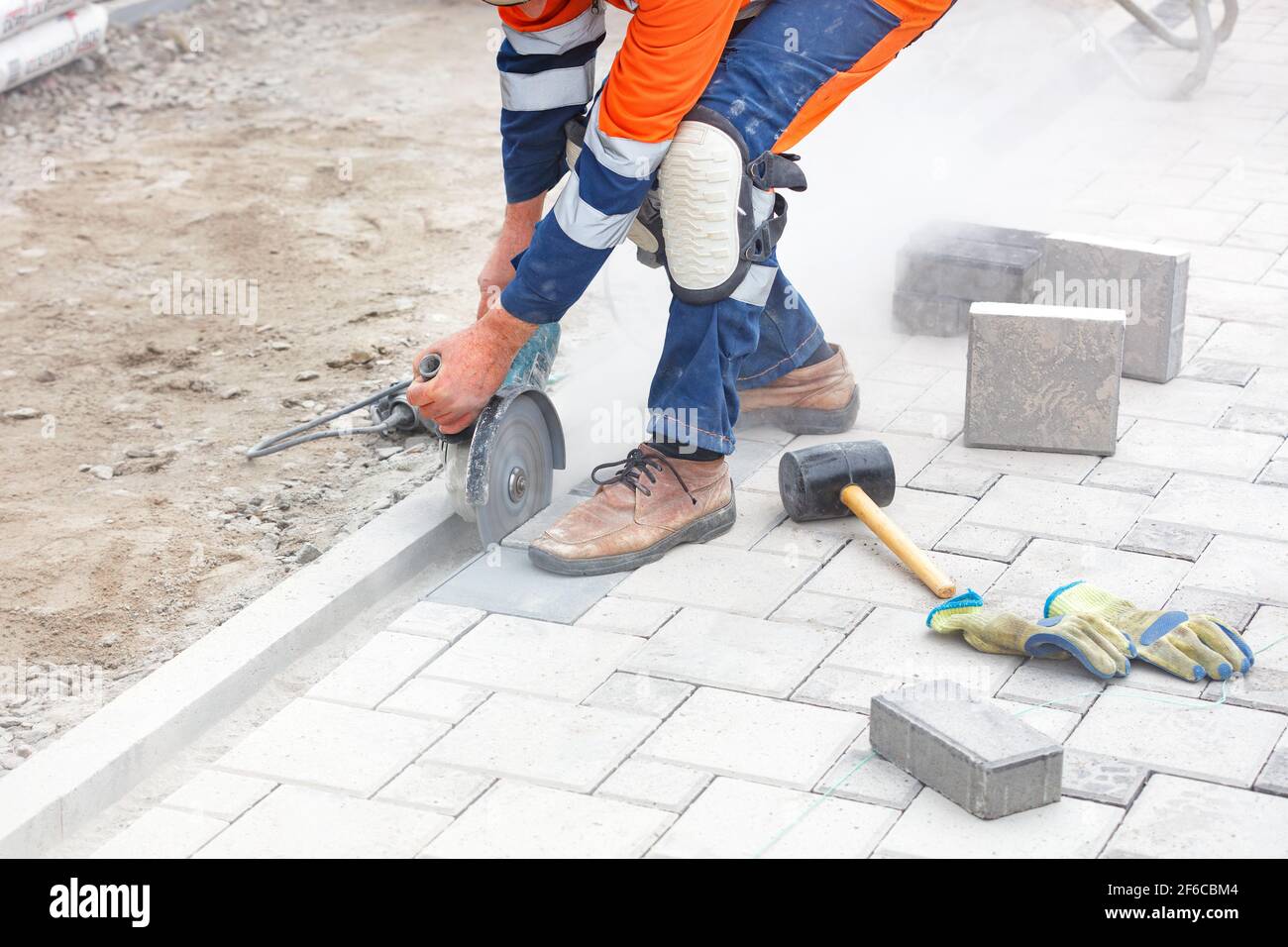 Un costruttore utilizza una smerigliatrice e un disco da taglio diamantato per tagliare le lastre di pavimentazione in una nuvola di polvere di cemento. Foto Stock
