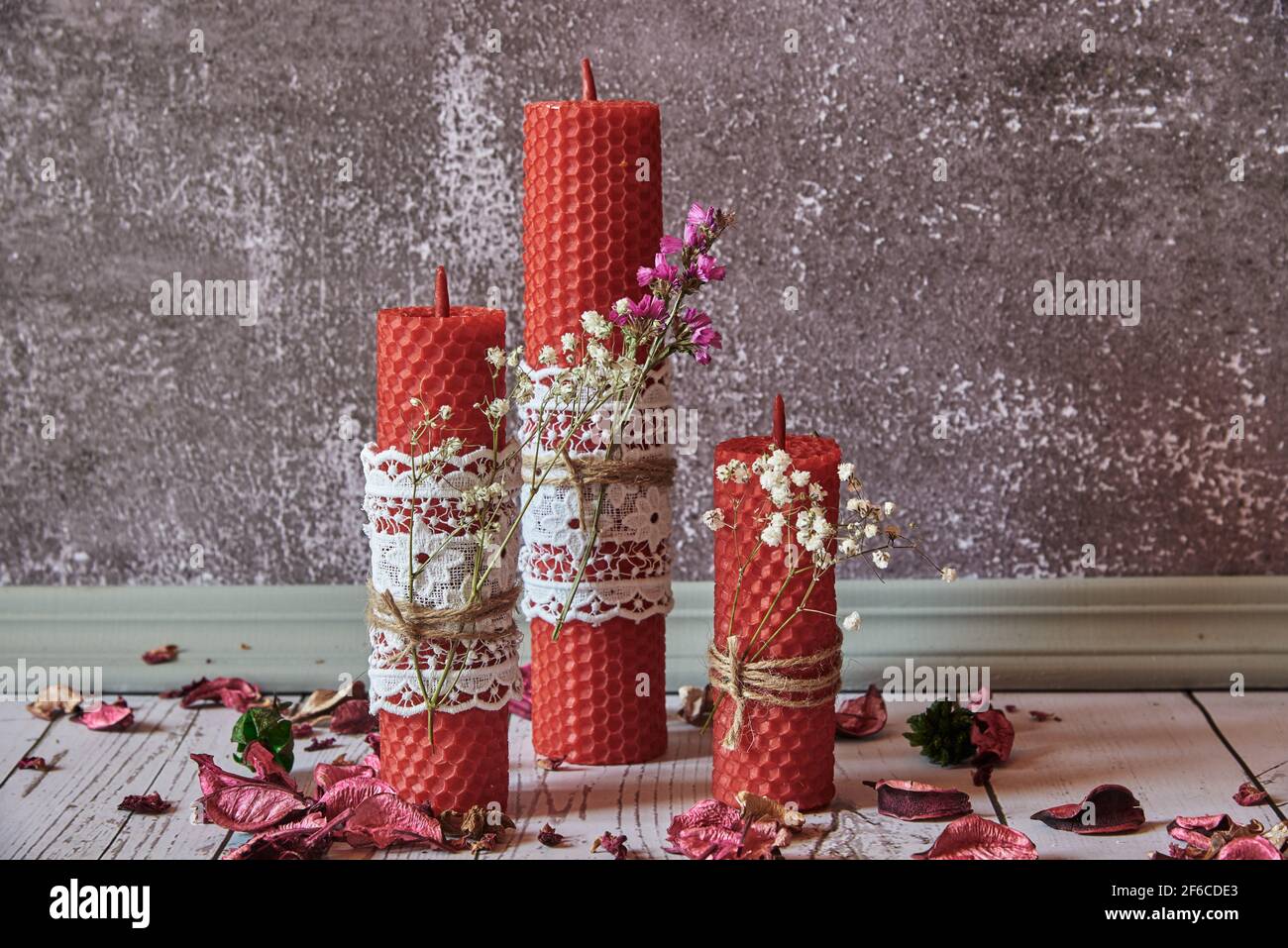 Tre candele di cera rossa fatte a mano, decorate con fiori e pizzi, su uno  sfondo grigio della parete. Elementi decorativi per la casa, prodotti  naturali biologici Foto stock - Alamy