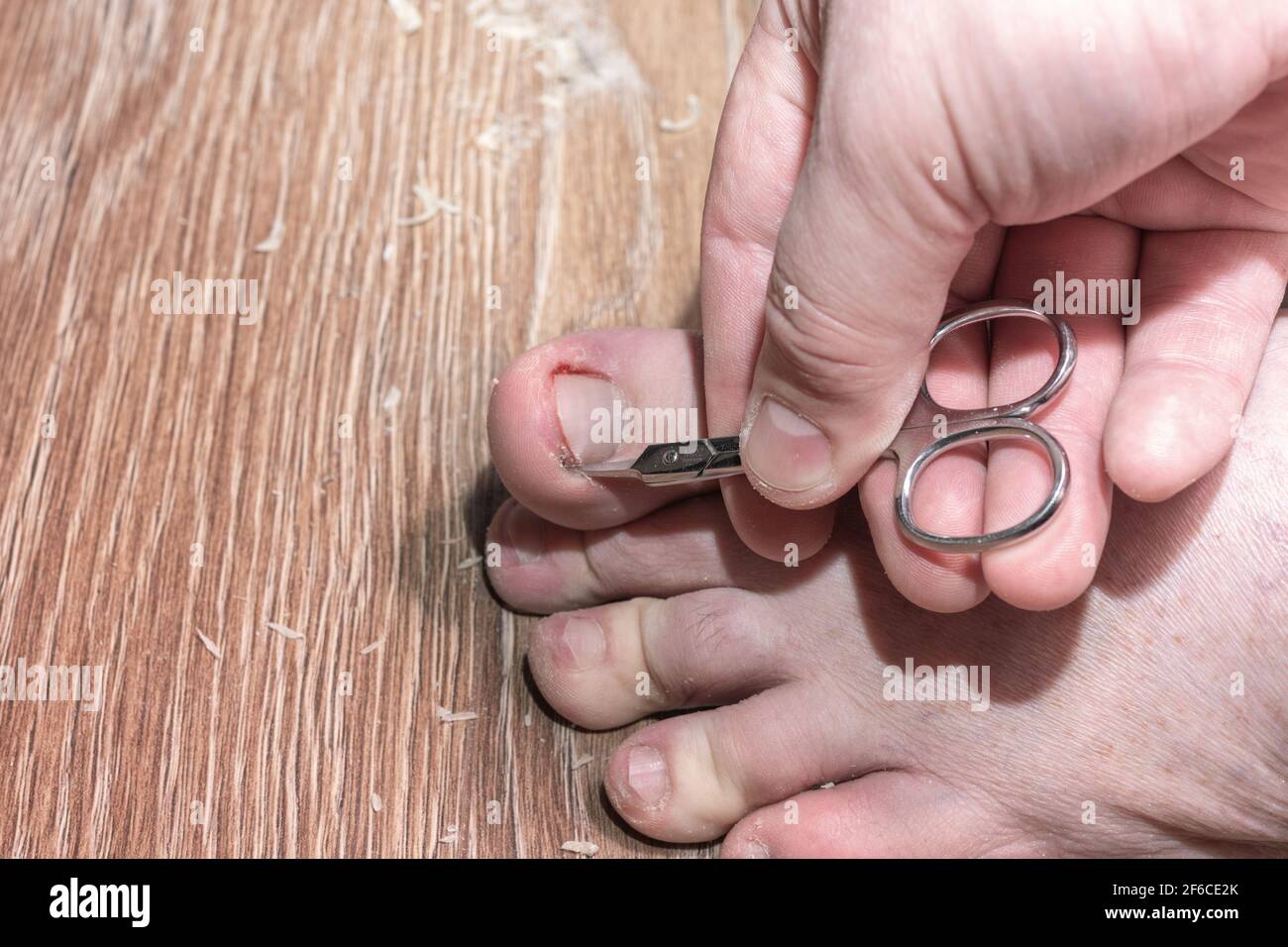 Primo piano di una mano che tiene una forbici per tagliare chiodi sulle dita dei piedi su uno sfondo di legno. Concetto di unghie sane. Pedicure del chiodo della punta. Cura delle unghie. Problemat Foto Stock