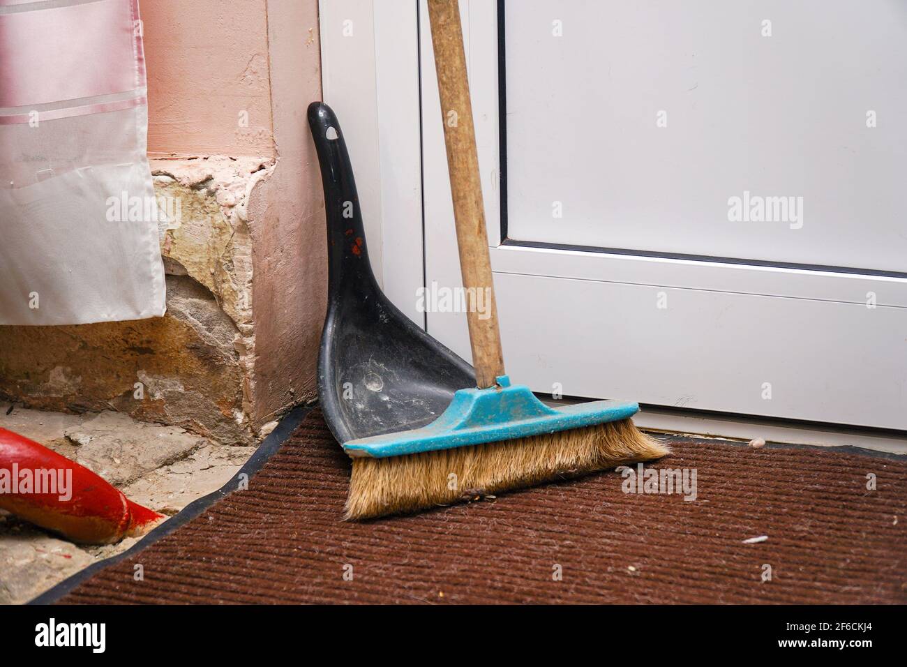 Una spazzola per spazzare il pavimento e un supporto per paletta in un angolo vicino alla porta Foto Stock