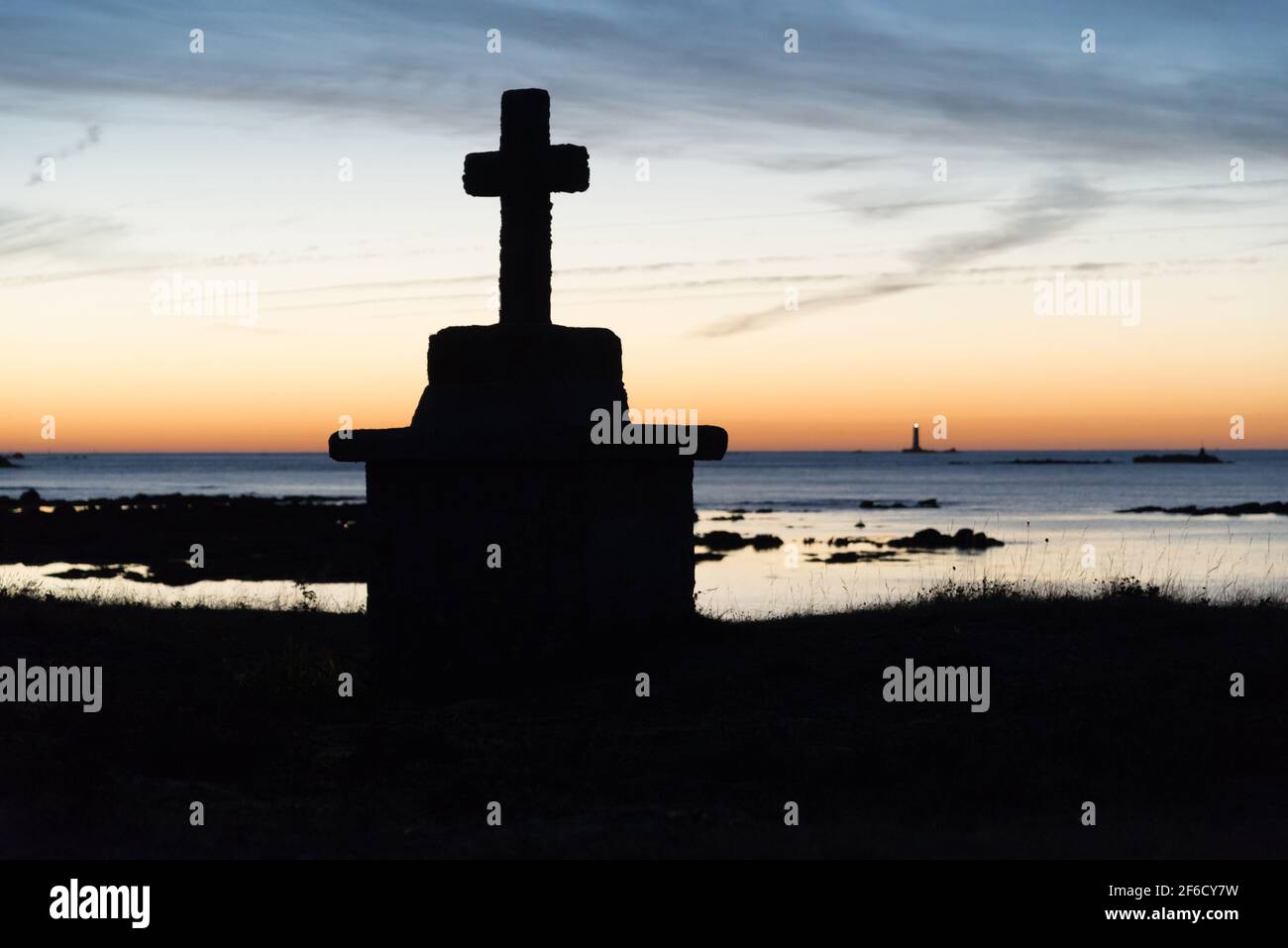 Croce monumento sulla spiaggia e faro in lontanissima terra sul mare durante l'alba sull'isola Hoedic, Francia Foto Stock
