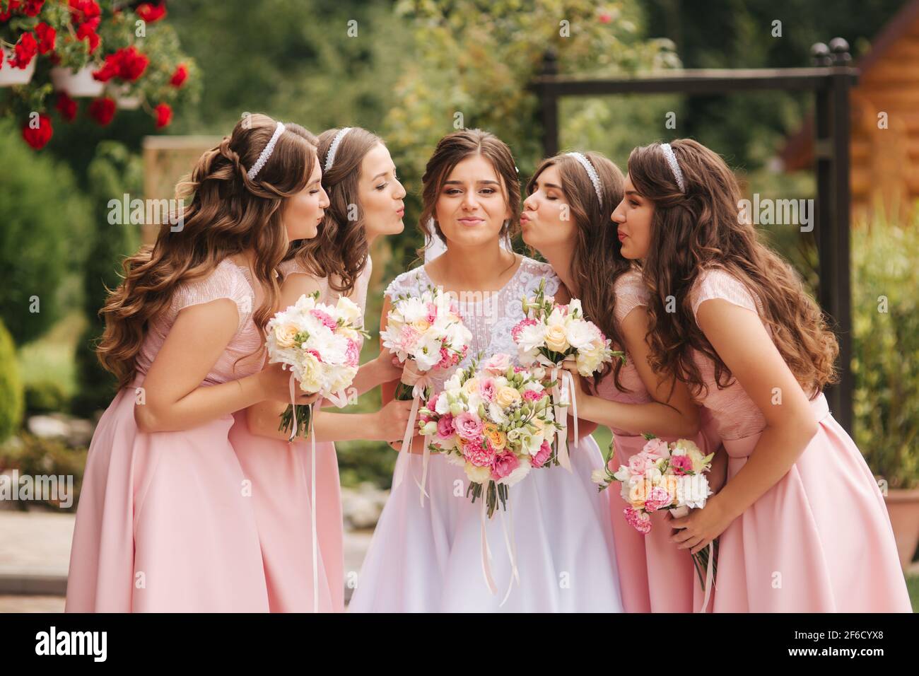 Buona sposa con bridesmaid tenere bouquet e divertirsi all'aperto. Bella bridesmaid negli stessi abiti stand vicino alla sposa affascinante in lungo abito da sposa Foto Stock