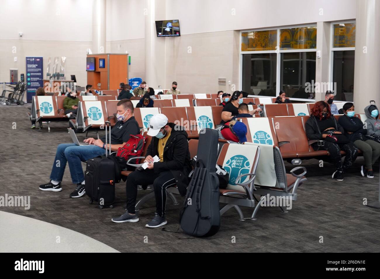 Le persone con maschere facciali si siedono tra segni marcatori di distanza fisici e sociali con le parole 'Say Safe. Lasciare spazio sui sedili nel Terminal B di Foto Stock