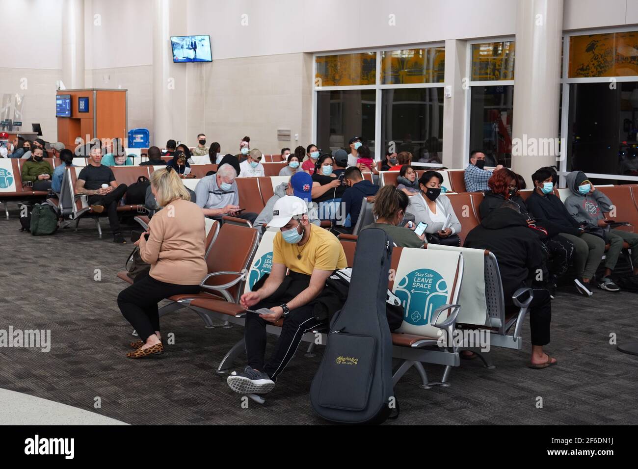 Le persone con maschere facciali si siedono tra segni marcatori di distanza fisici e sociali con le parole 'Say Safe. Lasciare spazio sui sedili nel Terminal B di Foto Stock