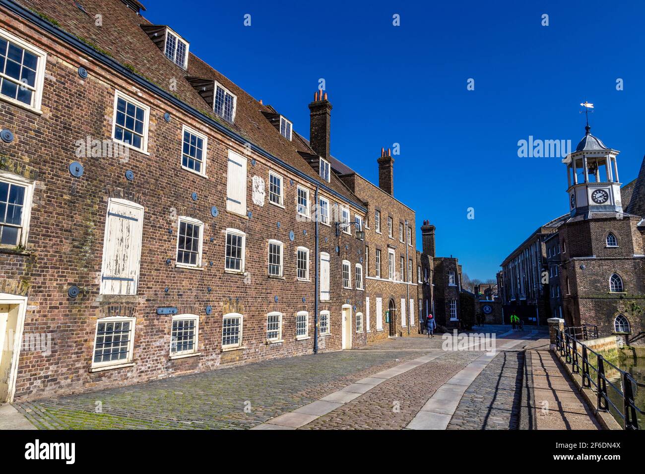Strada lastricata di ciottoli ed edifici in mattoni in Three Mills (House Mill, Miller's House e The Clock Mill) a Bow, Londra, Regno Unito Foto Stock