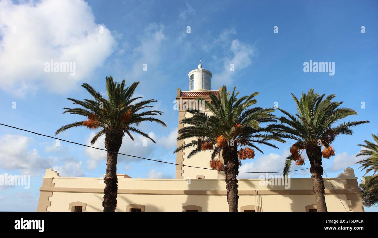 Faro Phare Cap Spartel con un cielo blu brillante con poche nuvole bianche. Palme da dattero che si trovano maestosamente di fronte alla struttura. Foto Stock