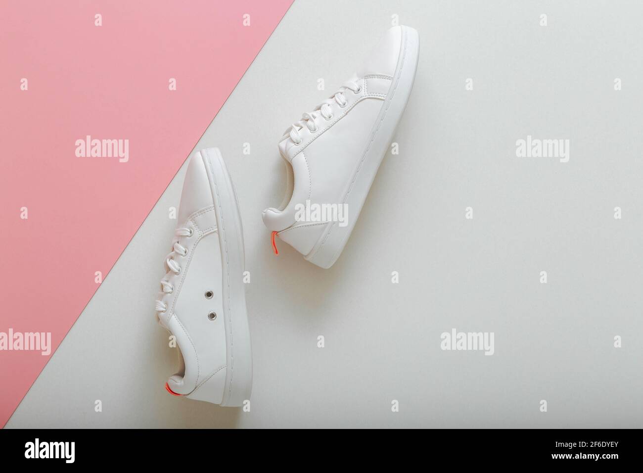 Sneakers bianche, scarpe femminili in pelle bianca con lacci su sfondo rosa. Paio di eleganti sneakers comode scarpe da donna hipper sportive. Vi Foto Stock