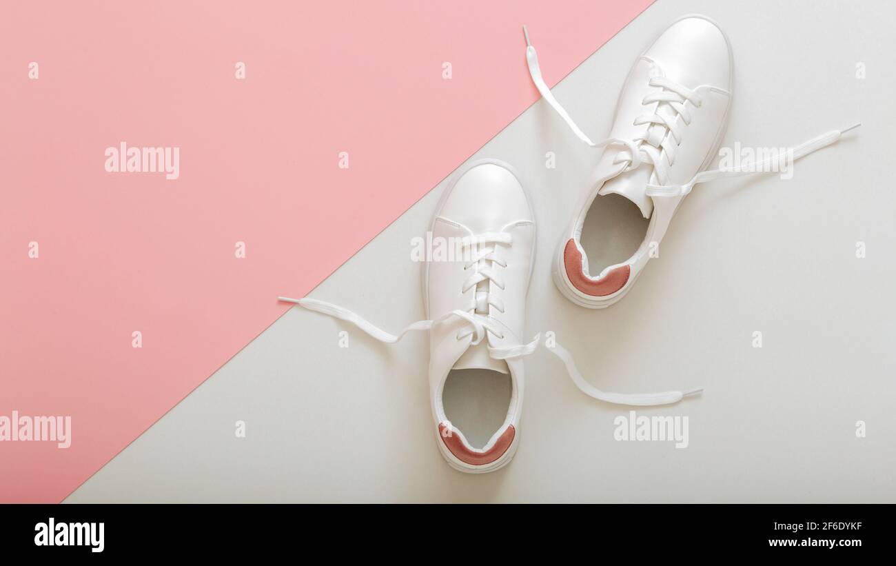 Sneaker bianche con lacci volanti, scarpe femminili in pelle bianca con lacci su sfondo rosa. Paio di eleganti sneakers comodo hipster wo sportivo Foto Stock