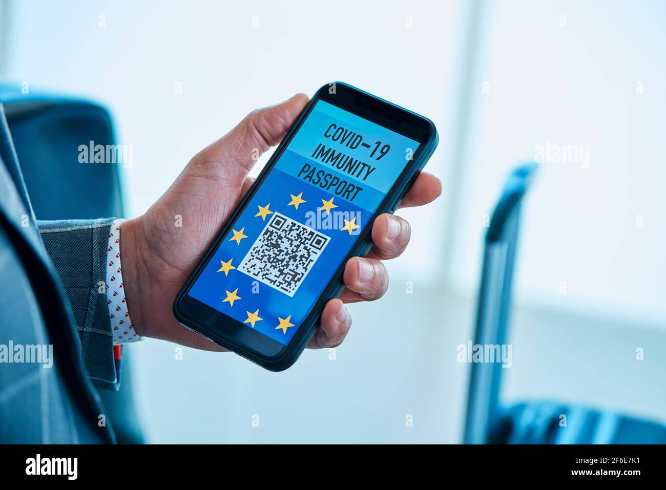closeup di un giovane uomo d'affari caucasico, in una tuta grigia, che ha un passaporto elettronico simulato europeo covid-19 immunità sullo schermo del suo intelligente Foto Stock