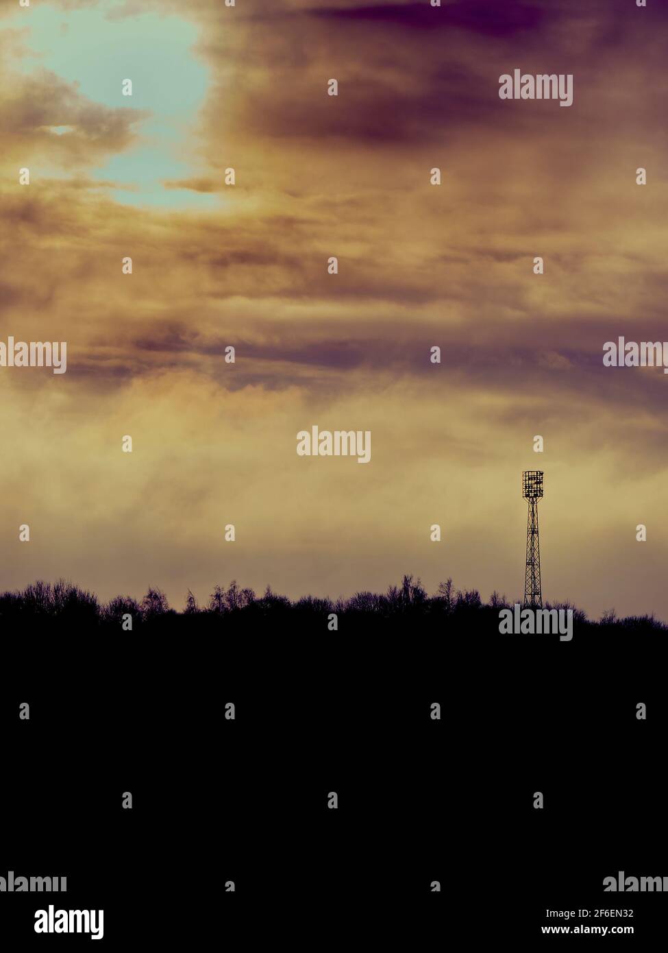 Un orizzonte dalla silhouette spettacolare con una torre a luce diffusa sopra una linea di alberi davanti a un intricato paesaggio torbido e a un protetto il sole scoppiando attraverso una lacerazione Foto Stock