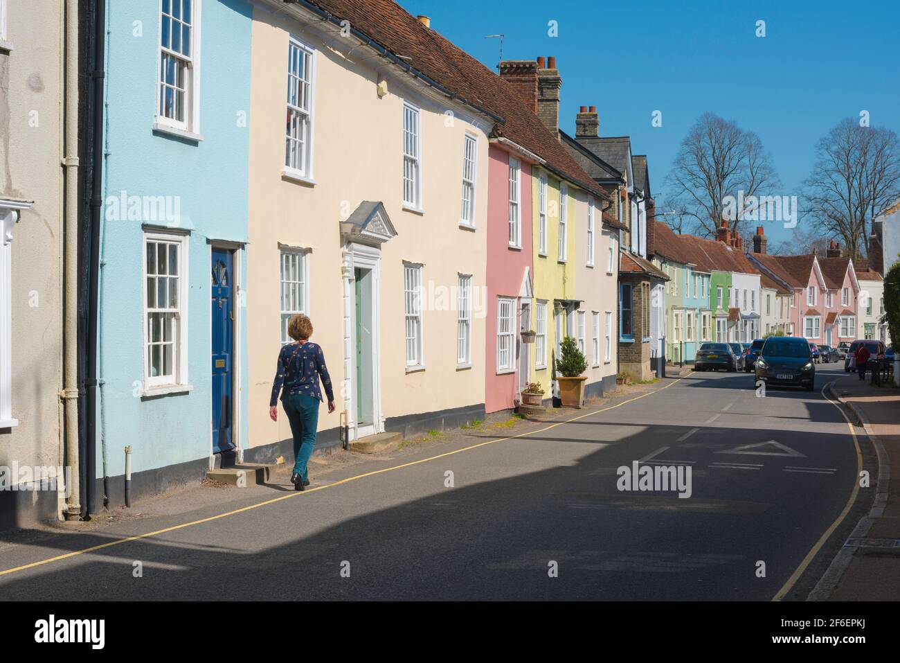 Strada tradizionale UK, vista posteriore di una donna che cammina lungo una strada villaggio tipicamente colorato contenente proprietà d'epoca, Coggeshall, Essex. Foto Stock