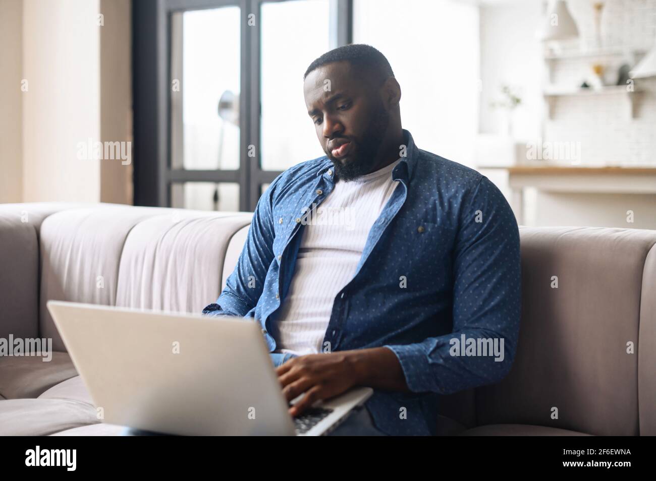 Afroamericano in abbigliamento casual utilizzando il computer portatile,  trascorre tempo libero online in rete seduto sul comodo divano, uomo nero  che lavora a distanza Foto stock - Alamy