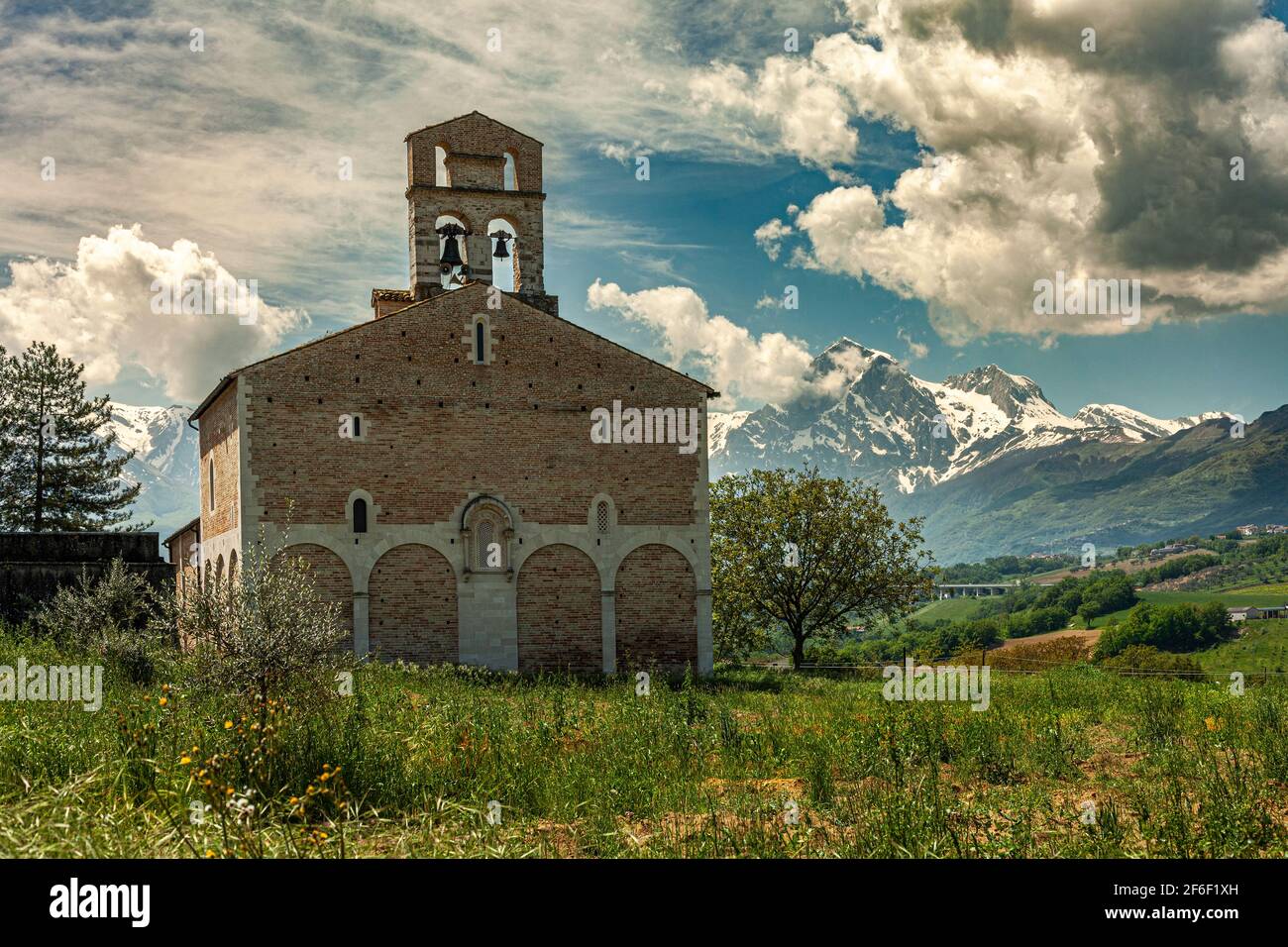 La chiesa di Santa Maria a Ronzano con le sue pareti in mattoni e gli archi ciechi in pietra. Sullo sfondo la catena del Gran Sasso con la neve. Abruzzo Foto Stock