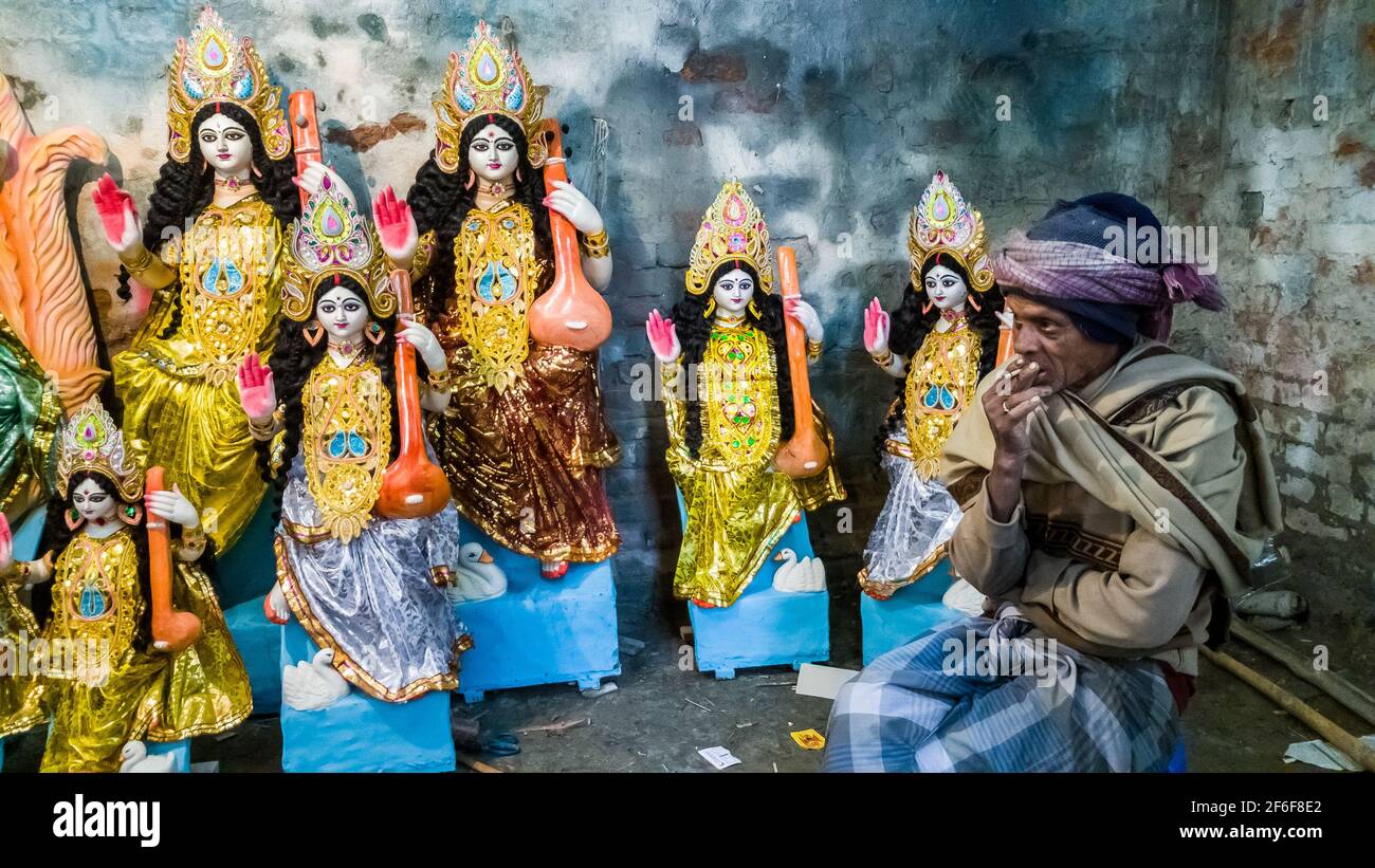 Kolkata, Bengala Occidentale, India - Gennaio 2018: Un anziano indiano che fuma un bidi al suo laboratorio di scultura con gli idoli della Dea Indù Durga su di Foto Stock